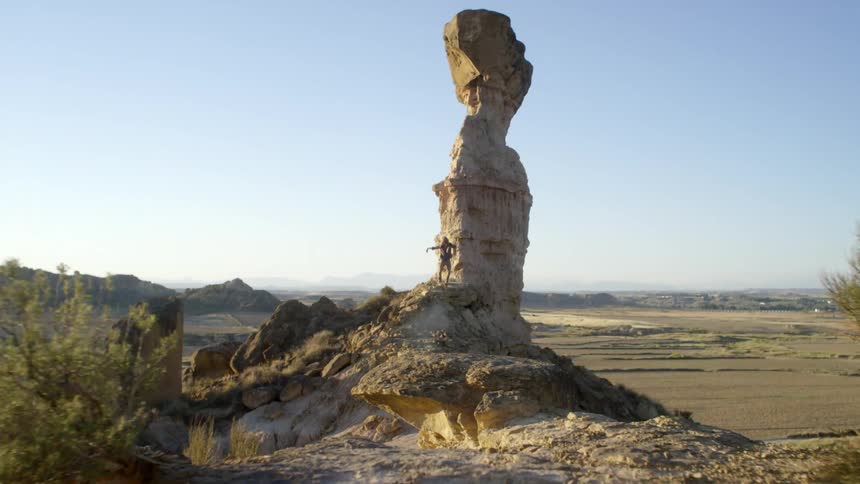 A man stands next to a very large rock and waves his arms in the air