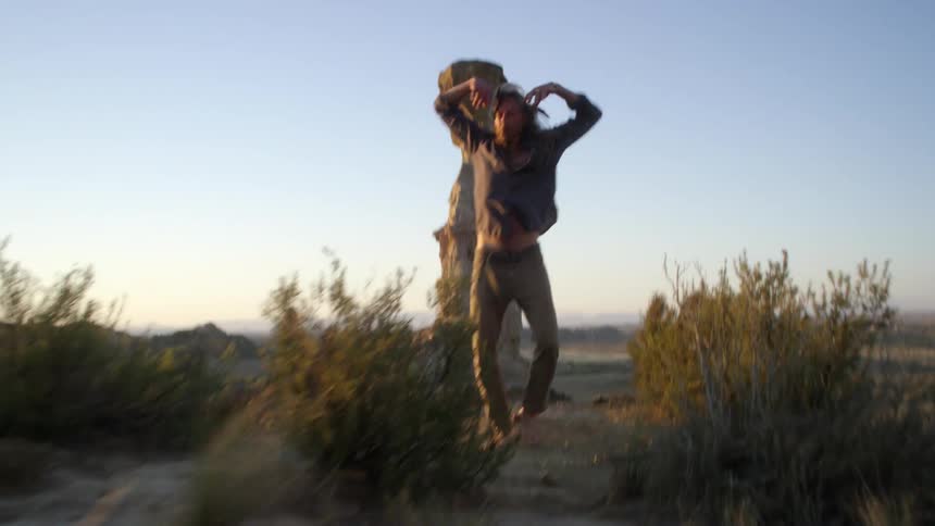 A man performs an aggressive dance while standing in a desert near a monument