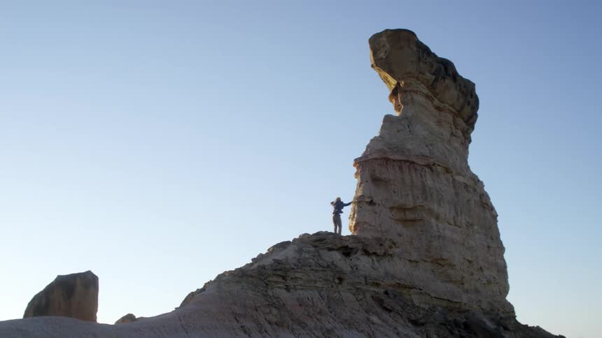 A man climbs up a small mountain and celebrates by dancing