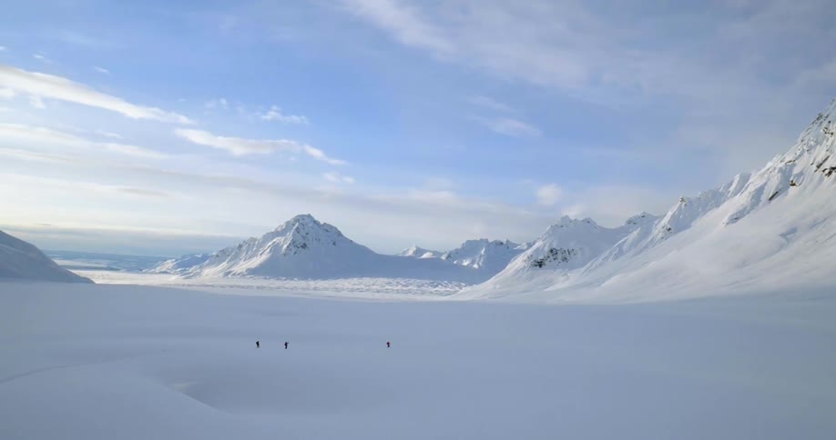 Aerial of three people moving through a snowy valley