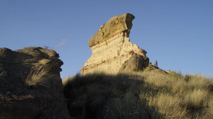 A rock formation with a grassy slope on a bright blue sky day