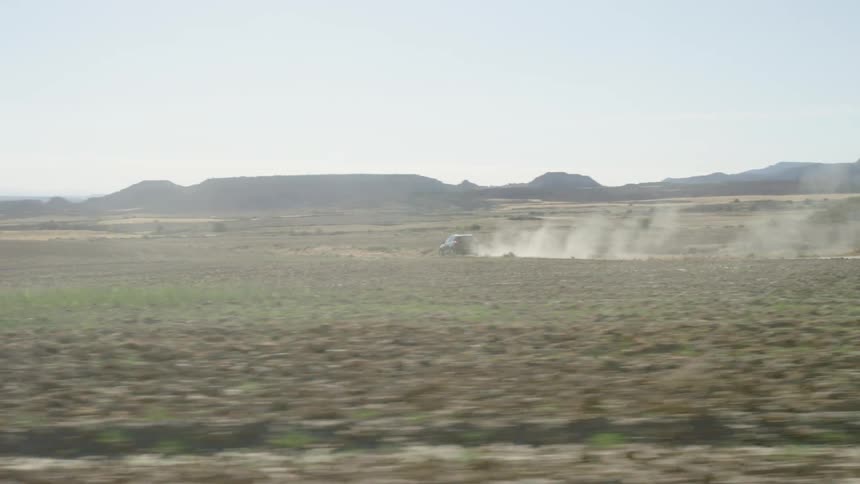 A vehicle kicks up a dust cloud as it drives through farm fields
