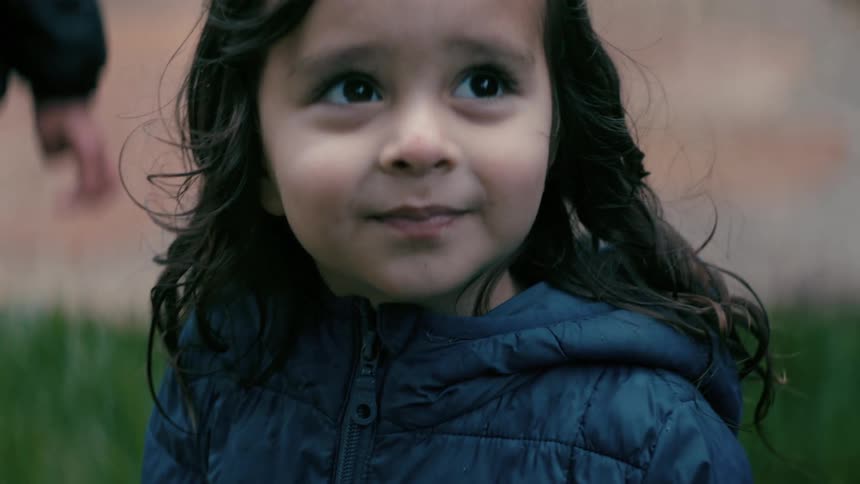 A little girl looks up towards the sky and opens her mouth and sticks her tongue out