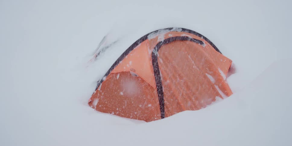 Snow falling heavily on and around a tent on snowy terrain