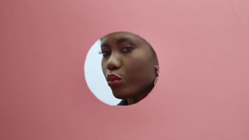 A woman looking through a hole in a pink wall and blowing a kiss