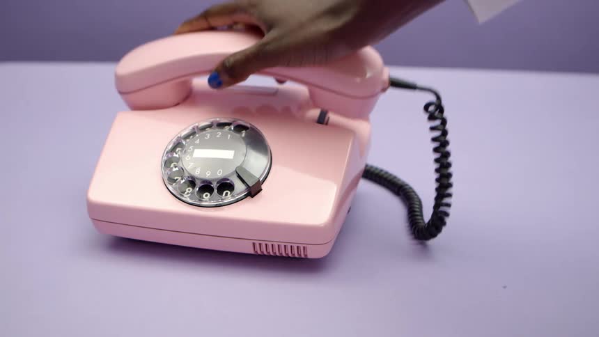 A woman picking up a receiver and hanging up a pink rotary phone