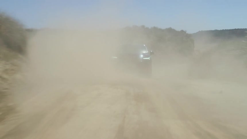 Dust and dirt blowing in the air as a car drives down a dirt road