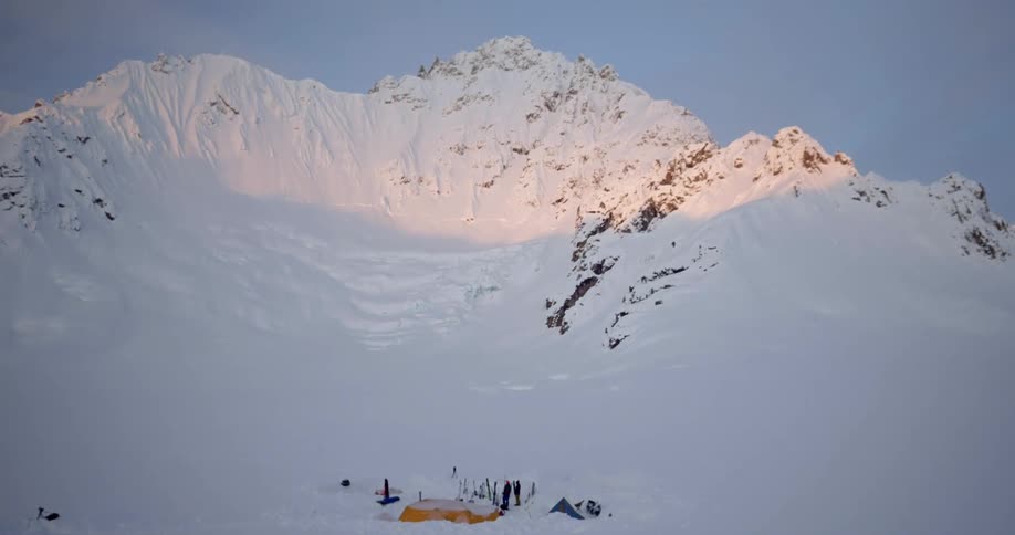 Aerial of people at a snowy campsite at the base of a mountain