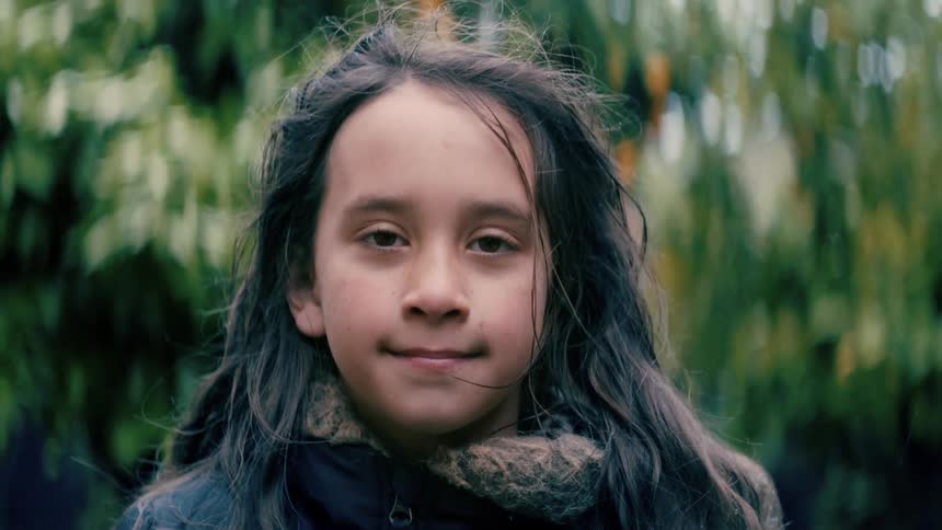 A girl looking into the camera while standing outdoors near vegetation