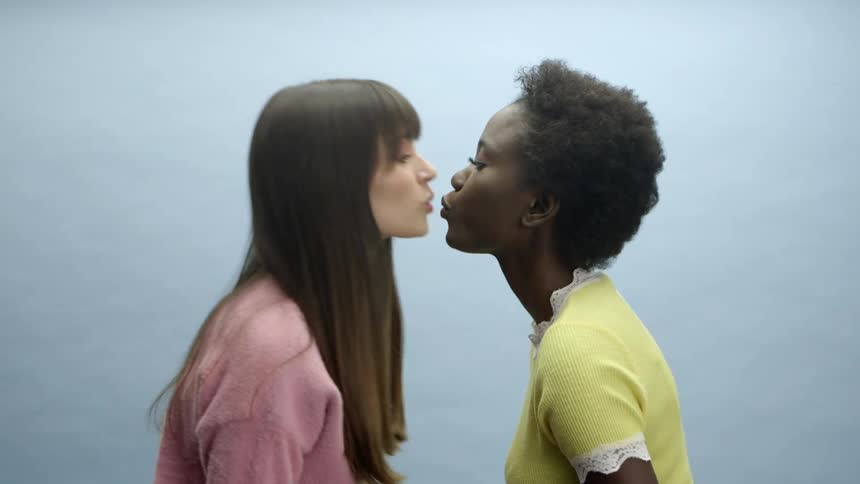 Two women lean forwards and kiss one another
