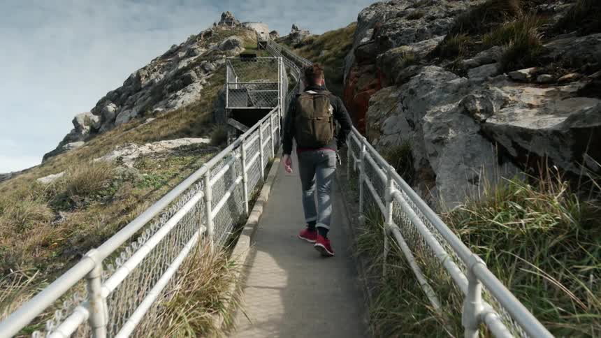 A man walks up a fenced path in the mountains