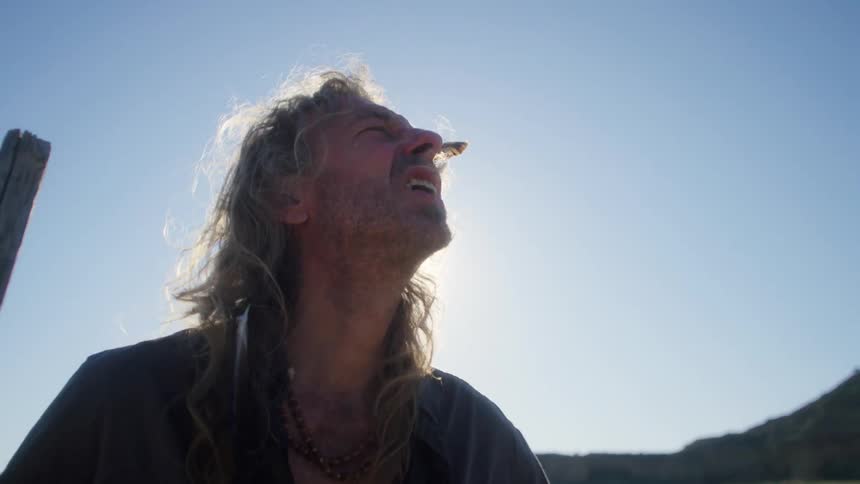 A man holding a walking stick catches his breath in the middle of a large field