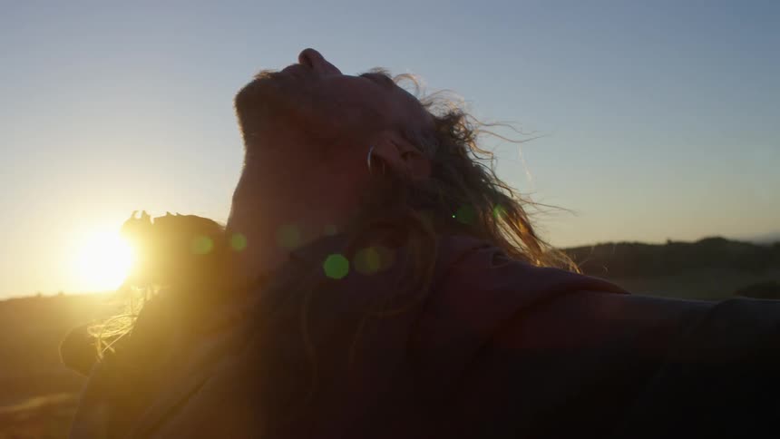 Man standing with arms wide open looking to the sky in the desert at sunset