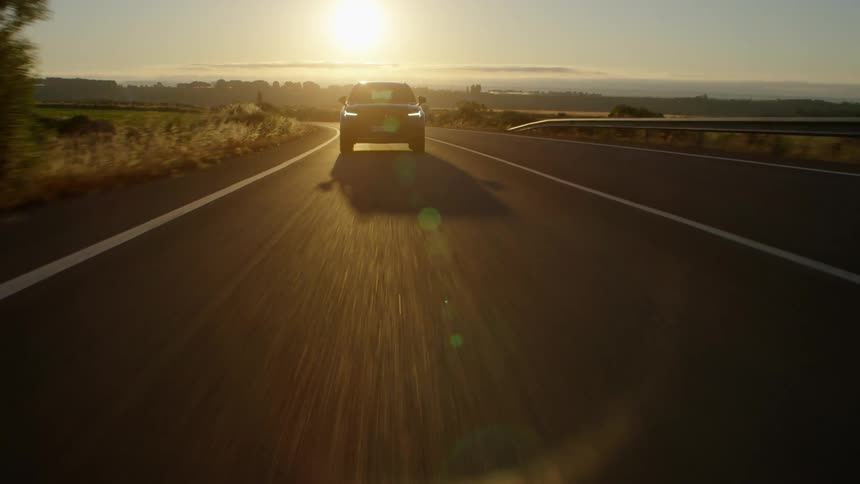 A vehicle driving on the road with the sky and the sun in the background