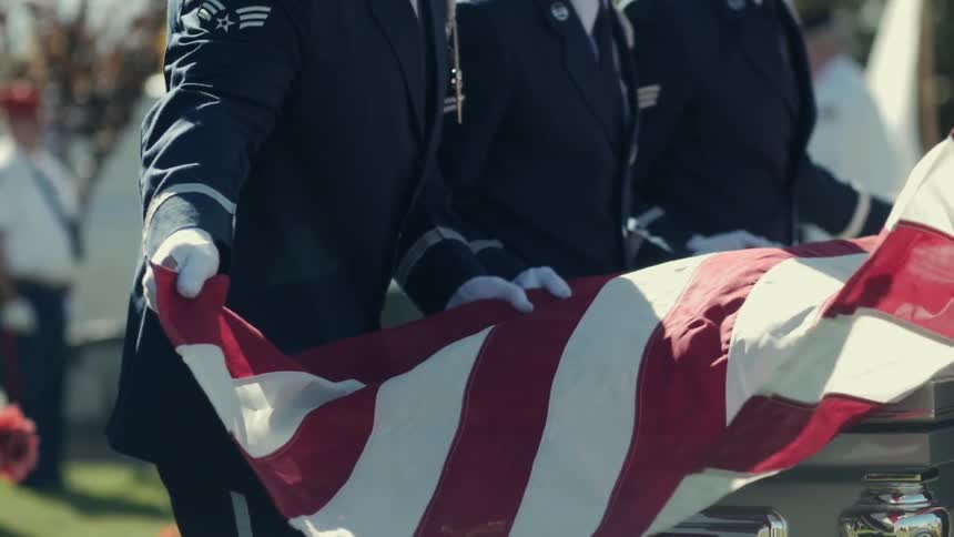Uniformed people place a flag over military coffin