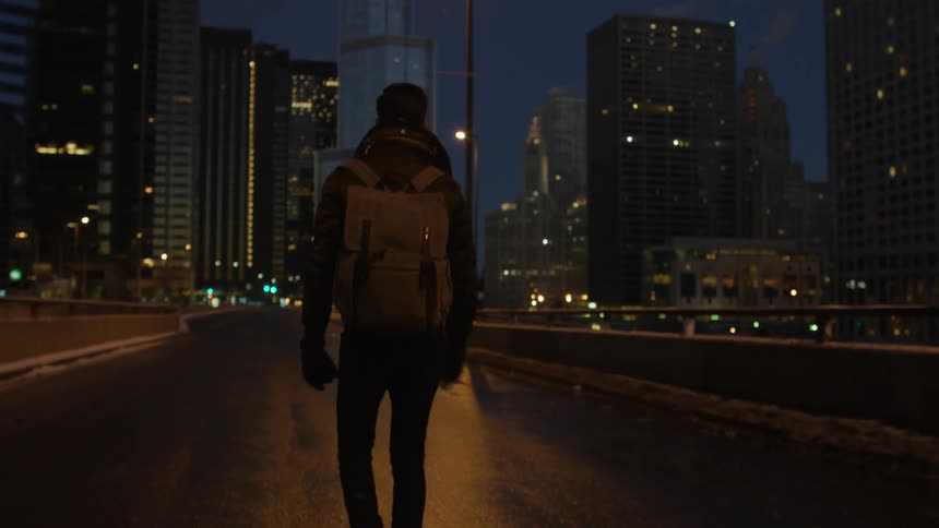A man is walking down a road at night towards a city