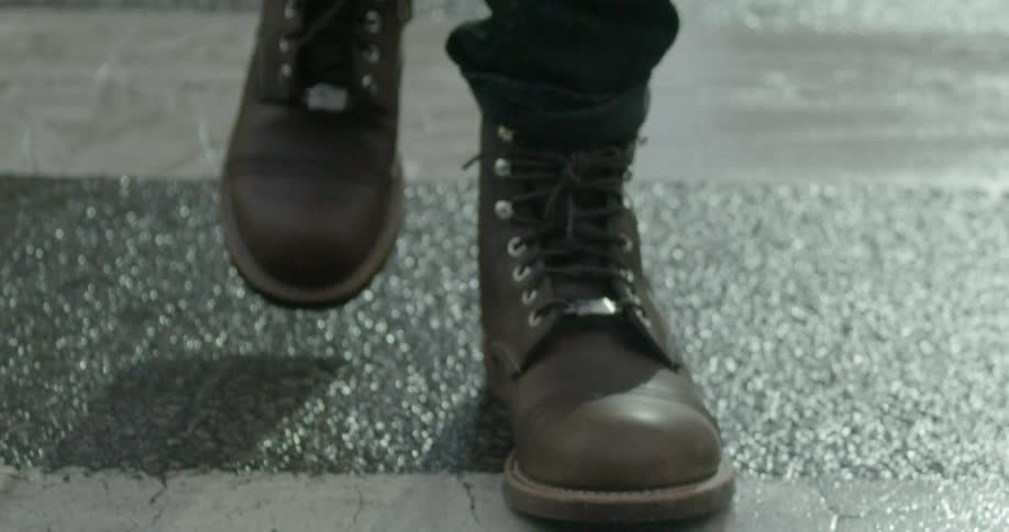 A person in boots crosses a wet street