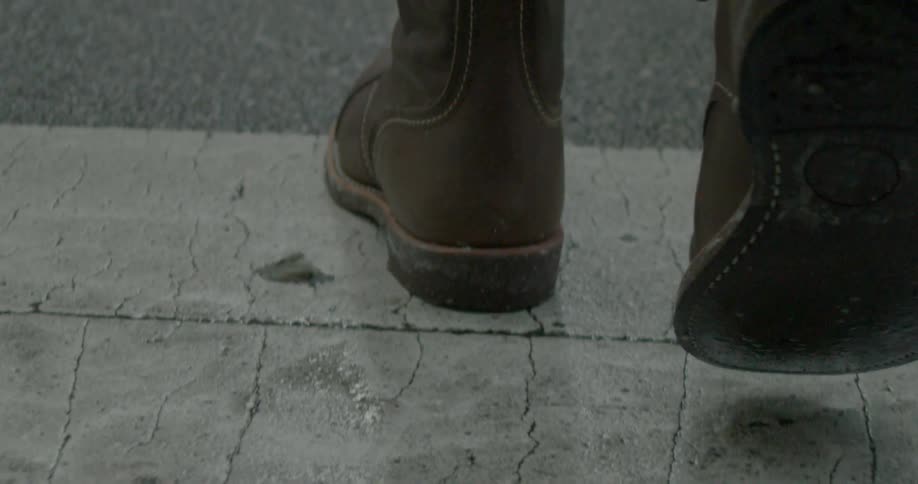 A person wearing boots is walking across a street
