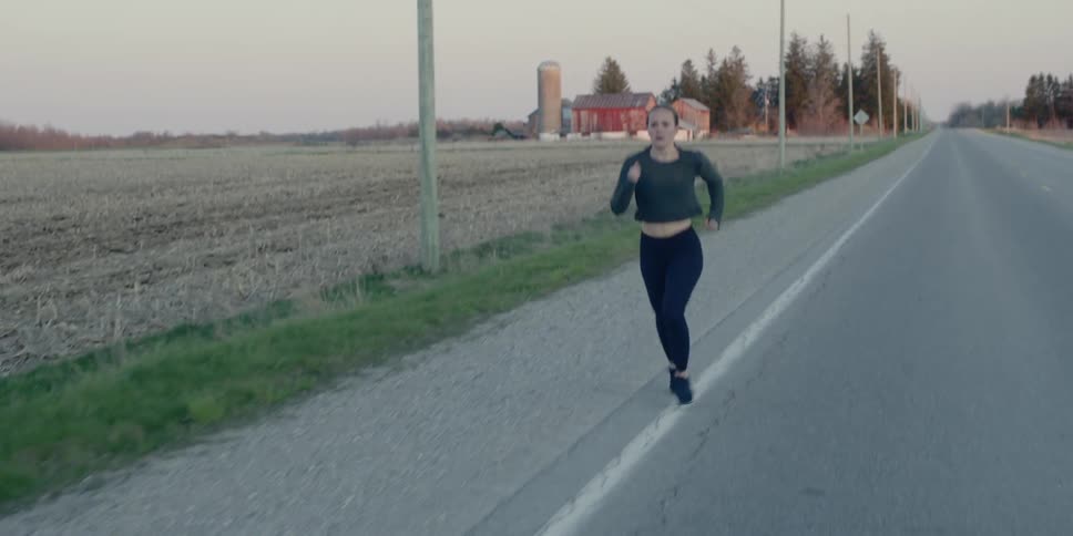 Woman runs along the asphalt road in the countryside