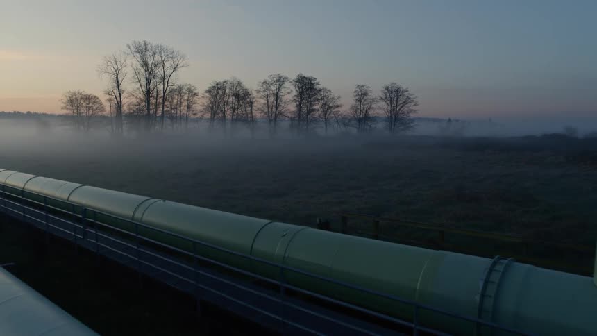 Pullback reveal of steel pipelines at first light near a delicate mist shrouded ecosystem