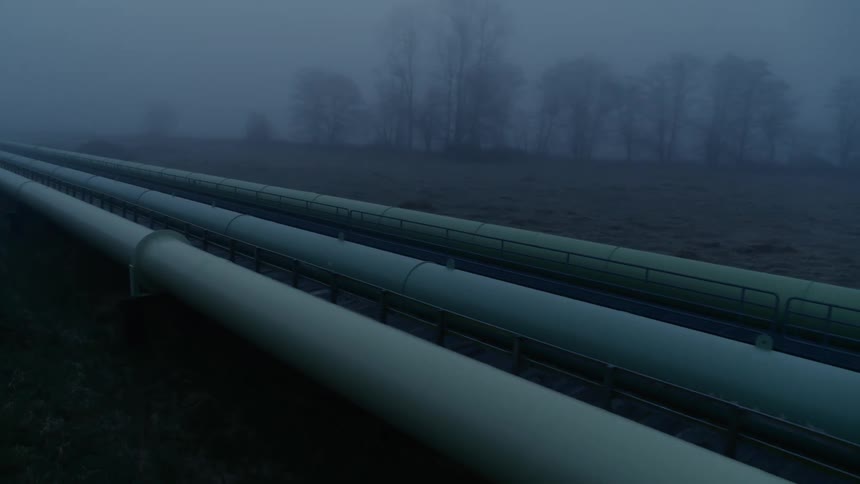 Large pipelines run parallel across a fog covered field at first light