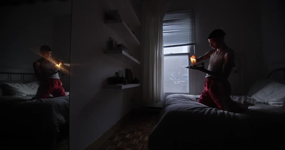 A teenager kneels on his bed and lights a candle