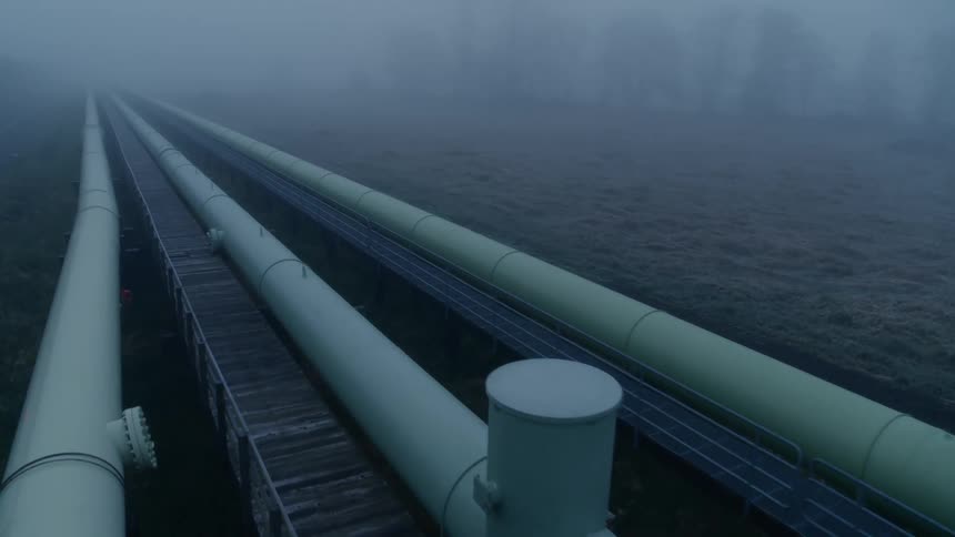 Flying above three pipelines that extend to the horizon along a fog shrouded landscape