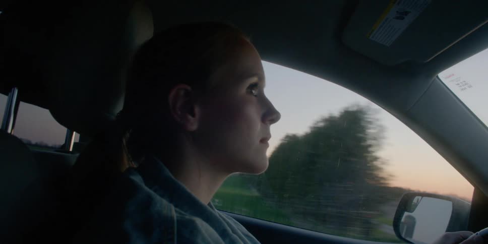 A woman driving a car with grassy fields in the background