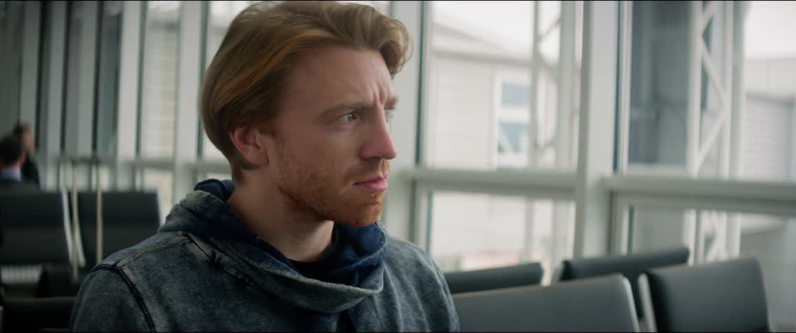 A man sitting in the waiting area of an airport turns to glance out the window