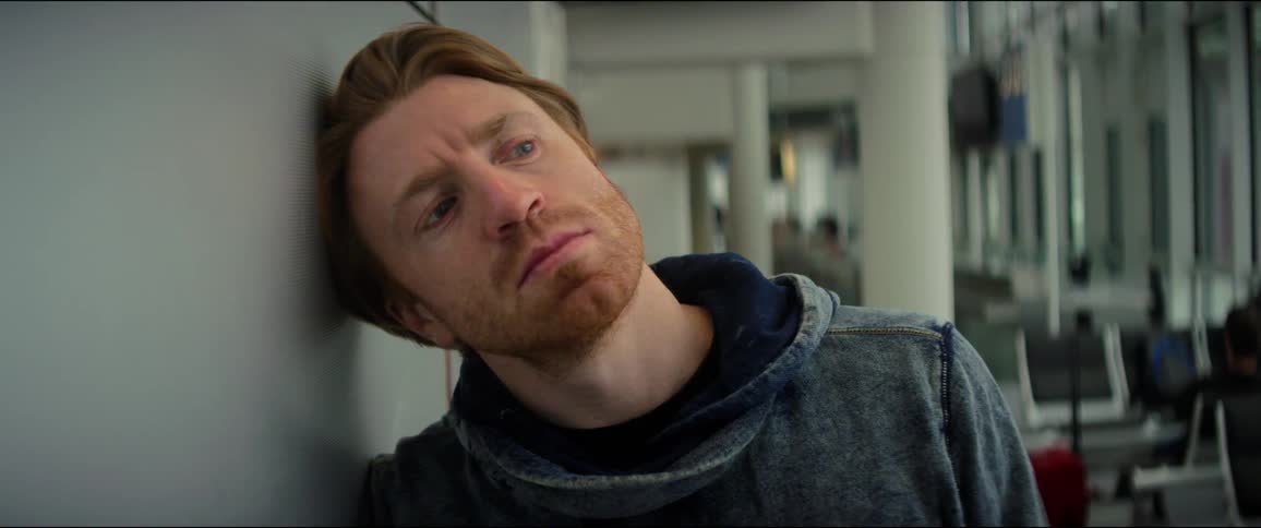 A man is bored as he stands with his against the wall in an airport
