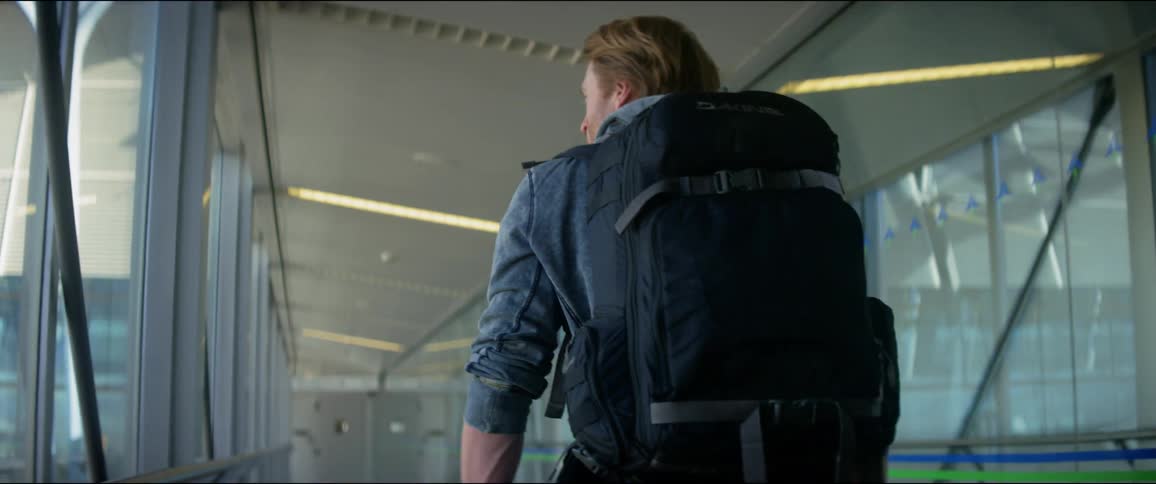 A man wearing a backpack walks down a pedestrian walkway connecting buildings and terminals