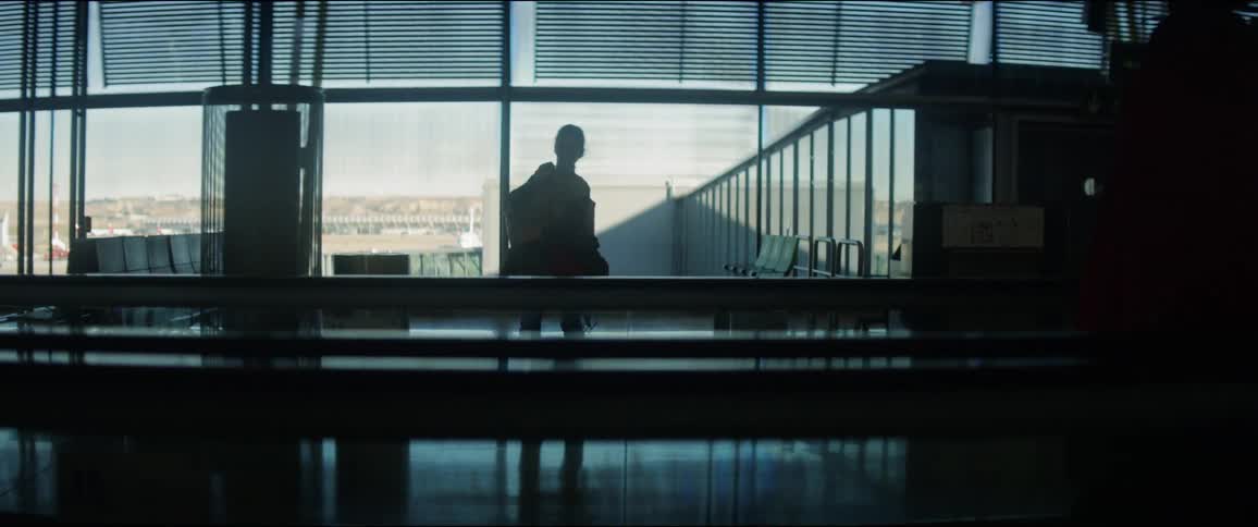 A silhouette of a woman walking in an airport with two people in the foreground on a conveyor belt