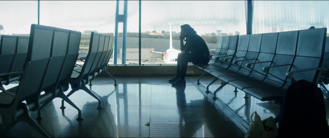 A man sitting alone shrouded in shadow in the dim waiting area of an airport