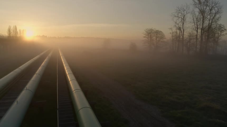 Flying over a pipeline network as the sun rises over fog shrouded hills in the distance