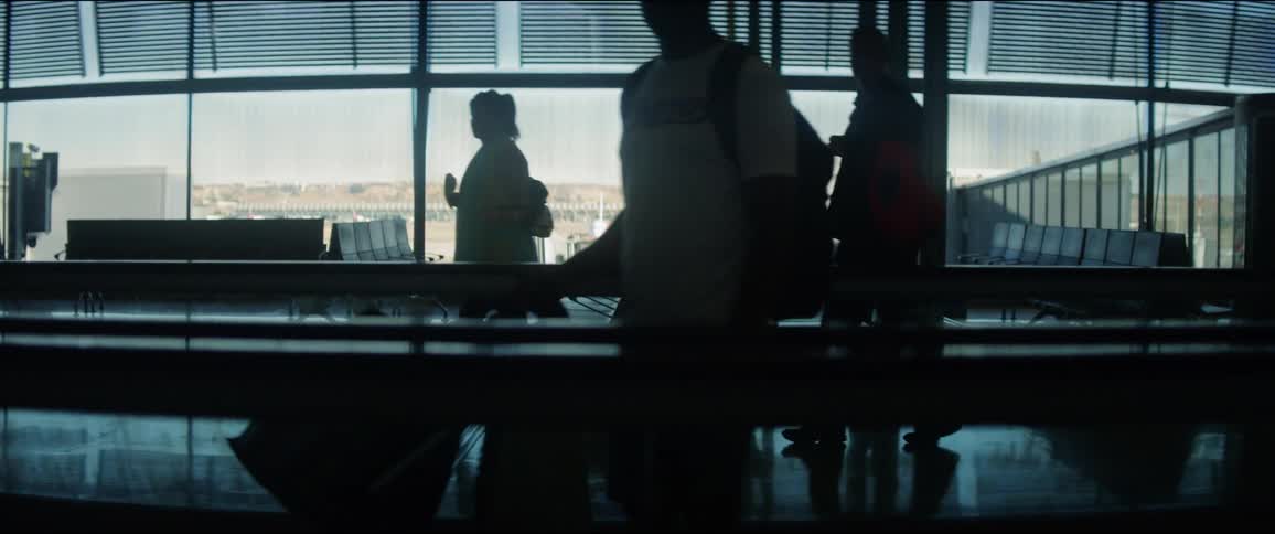 Passengers move through the airport using the moving sidewalk and normal walkway area while carrying their luggage