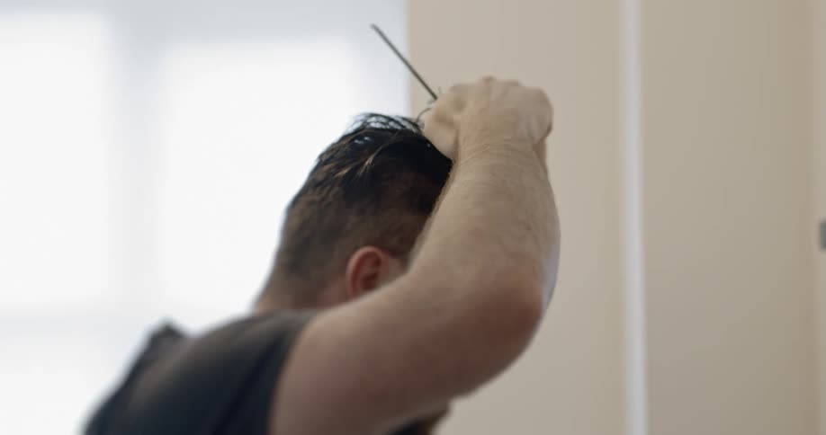 A man lifts up his hair as he prepares to cut it during isolation