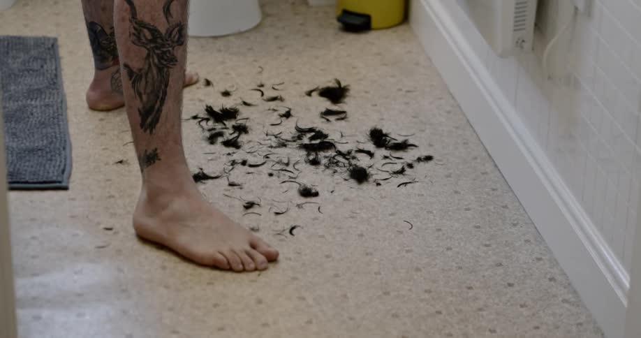 A man stands in hair that he has shaved off his head