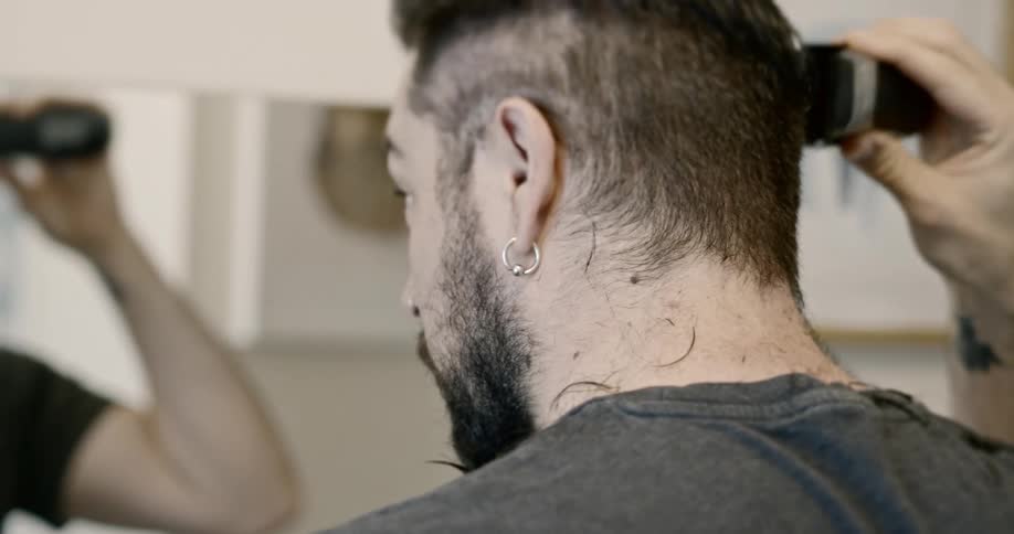 A man shaves his head in front of a mirror during COVID19 lockdown