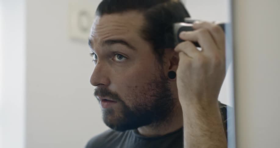 A white man shaves his hair with an electric razor during COVID lockdown
