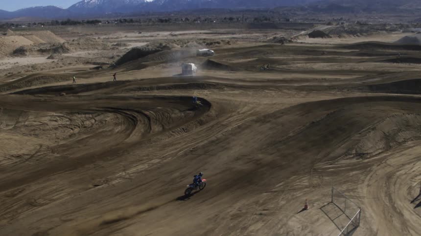 Dirt bikes move along uneven dirt course with mountains on the horizon