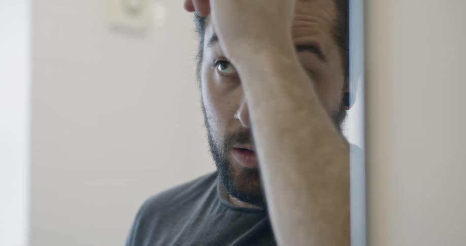 A white man combs his hair in front of a mirror