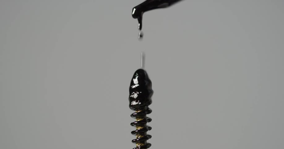 A dropper drops a black substance over a screw