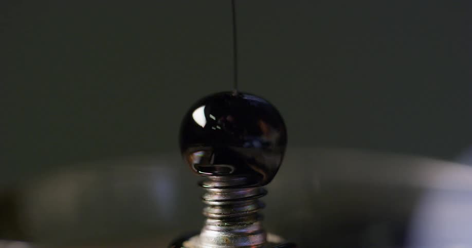 Black liquid is poured on a screw and forms a sphere