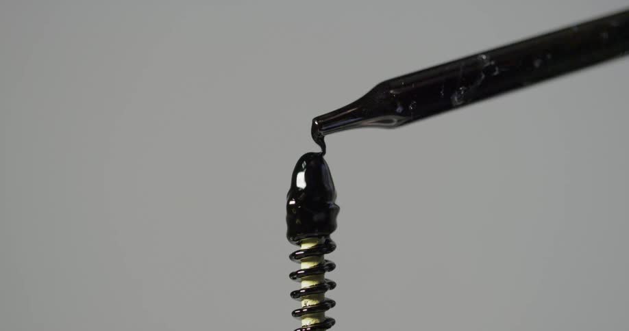 A dropper is used to drip black ink on a pin and spring covering it