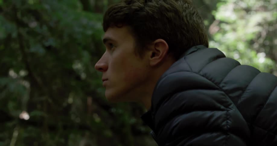 Man stooping down raises his head and takes a breath in the forest