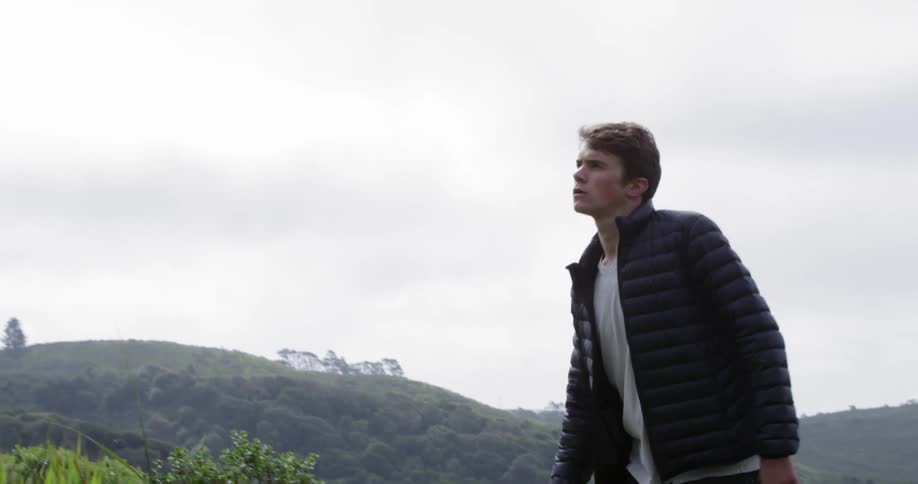 A young man is walking up a steep hill next to a forested area