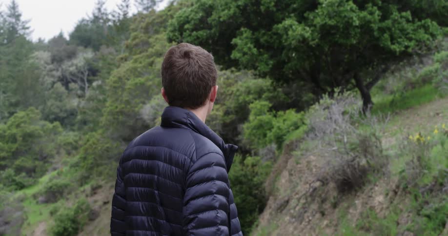 Man in a puffer jacket standing in a forest looking around