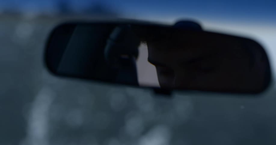A teenage boy can be seen in the rear view mirror of his car