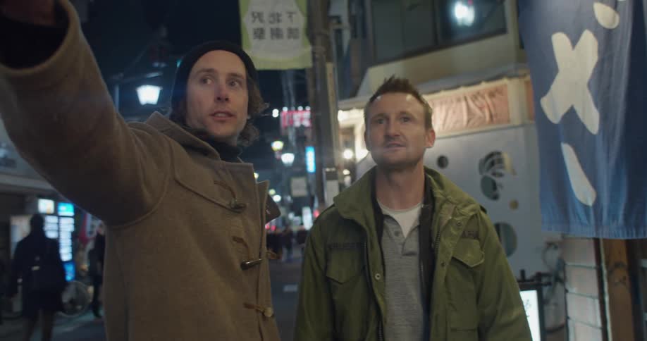 Two friends stand in a city street talking and pointing
