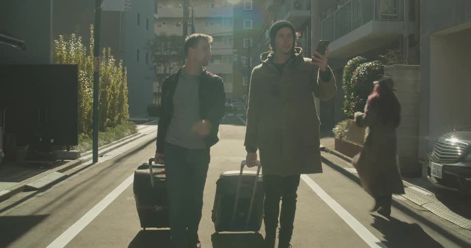 Two white males roll their luggage down a narrow neighborhood street